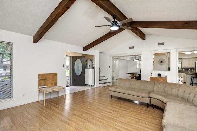 living room featuring light hardwood / wood-style floors, ceiling fan, a textured ceiling, and vaulted ceiling with beams