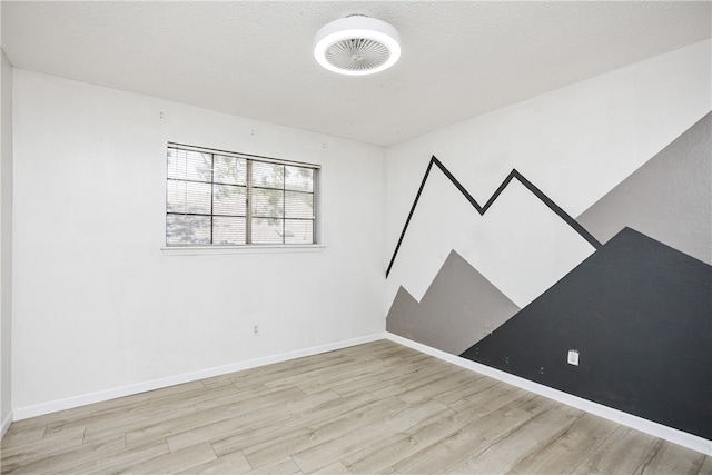 empty room with light wood-type flooring and a textured ceiling