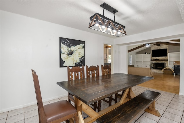 tiled dining room featuring built in shelves, a textured ceiling, a brick fireplace, lofted ceiling, and ceiling fan