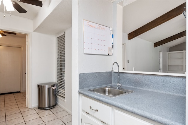 kitchen featuring light tile patterned flooring, sink, ceiling fan, vaulted ceiling with beams, and white cabinets