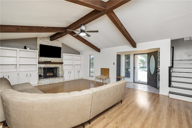 living room with vaulted ceiling with beams, a textured ceiling, a brick fireplace, ceiling fan, and light hardwood / wood-style flooring