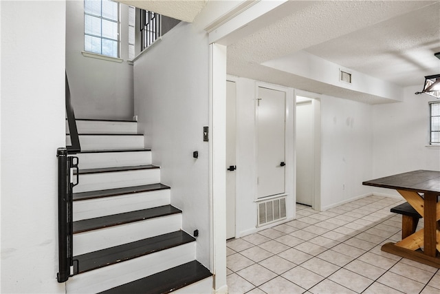 stairway with a textured ceiling and tile patterned flooring