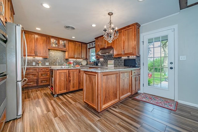 161 Red Bird Rdg, Beeville, TX 78102 - kitchen with under cabinet range hood, freestanding refrigerator, brown cabinets, a chandelier, and decorative backsplash
