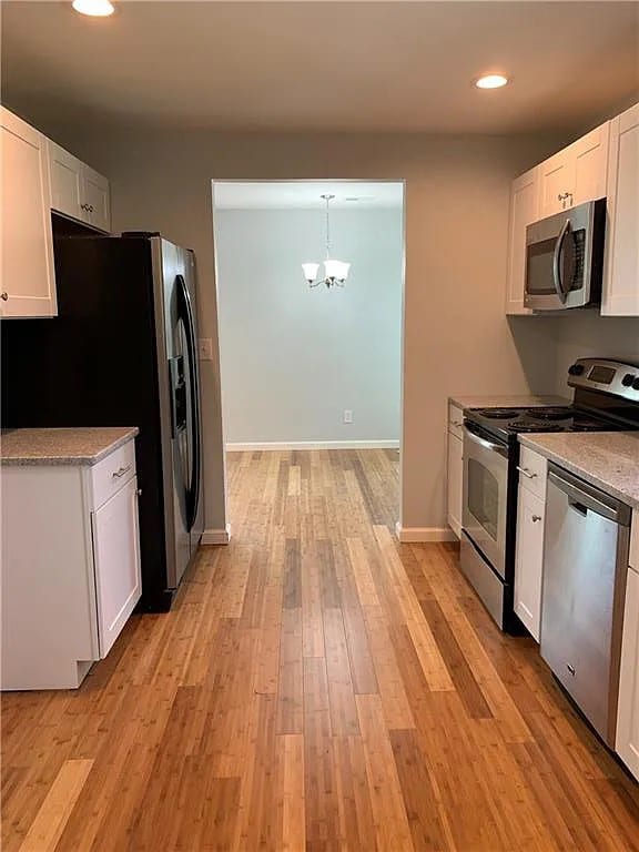 kitchen featuring white cabinets, light hardwood / wood-style floors, pendant lighting, and appliances with stainless steel finishes