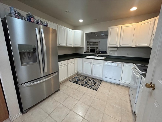 kitchen featuring dark countertops, recessed lighting, white cabinetry, a sink, and white appliances