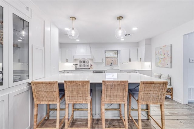 kitchen featuring decorative light fixtures, a breakfast bar, custom range hood, white cabinets, and sink