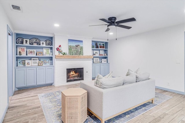 living room featuring a brick fireplace, light wood-type flooring, built in features, and ceiling fan