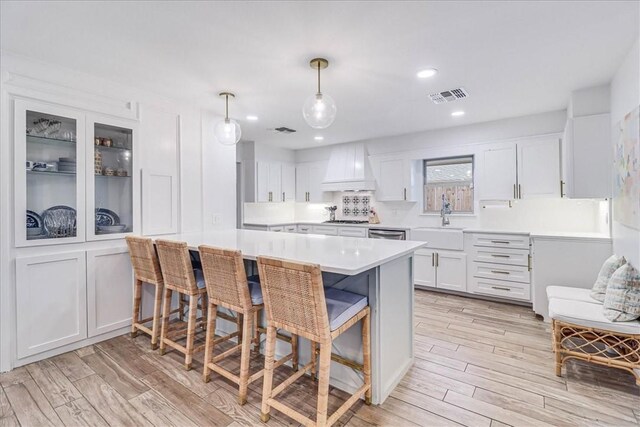 kitchen with premium range hood, pendant lighting, a breakfast bar, sink, and white cabinets