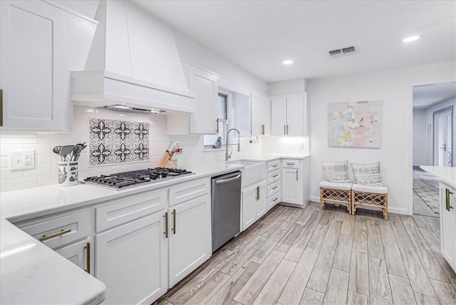 kitchen with appliances with stainless steel finishes, white cabinets, sink, and custom range hood