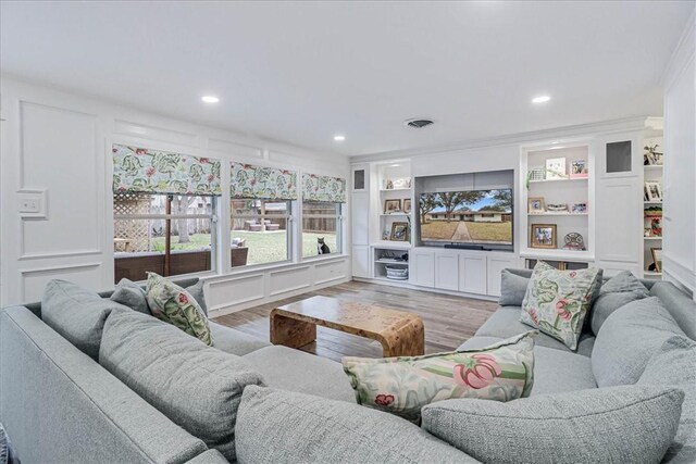 living room featuring ornamental molding, light hardwood / wood-style flooring, and built in shelves