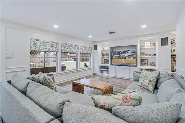 living room with built in shelves, light hardwood / wood-style flooring, and ornamental molding