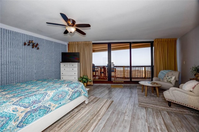 bedroom featuring hardwood / wood-style floors, access to outside, ceiling fan, and a wall of windows