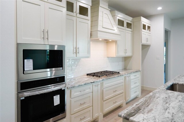 3525 Sahar Lk, Corpus Christi, TX 78380 - kitchen with tasteful backsplash, light wood-style floors, light stone countertops, custom range hood, and stainless steel appliances
