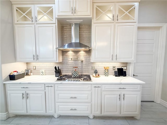 8137 Berenstain Dr, Corpus Christi, TX 78414 - kitchen featuring wall chimney range hood, stainless steel gas stovetop, decorative backsplash, and glass insert cabinets
