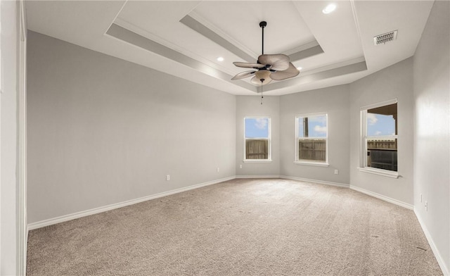 carpeted empty room featuring visible vents, a tray ceiling, ceiling fan, and baseboards