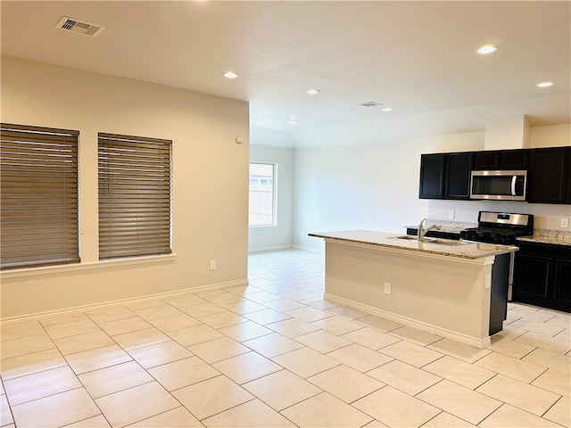 kitchen with stainless steel appliances, light stone counters, sink, light tile patterned floors, and a kitchen island with sink