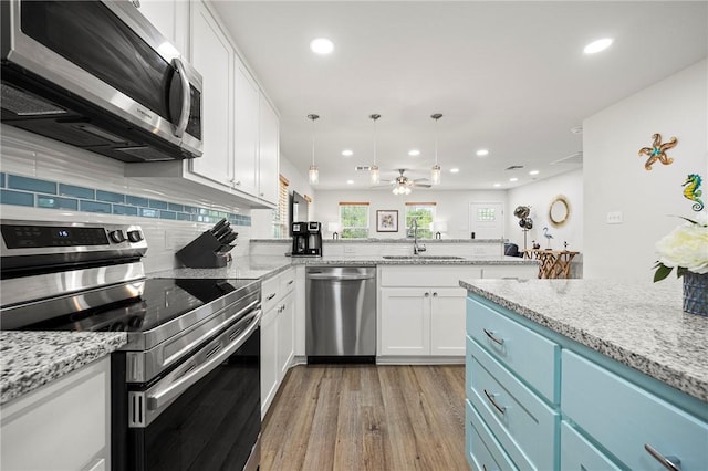 607 Huisache Lane, Ingleside On The Bay, TX 78362 - kitchen featuring appliances with stainless steel finishes, a sink, light wood-type flooring, blue cabinets, and a peninsula