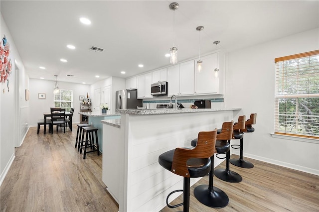 607 Huisache Lane, Ingleside On The Bay, TX 78362 - kitchen featuring stainless steel appliances, a kitchen bar, light wood-style floors, white cabinetry, and baseboards