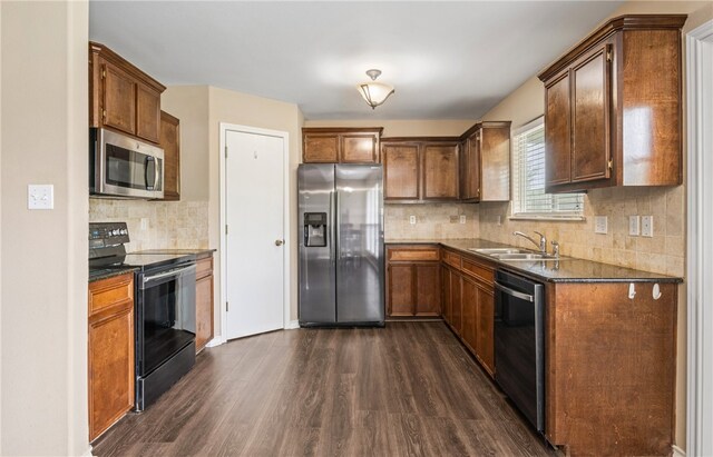 kitchen featuring dark countertops, a sink, stainless steel appliances, backsplash, and dark wood-type flooring