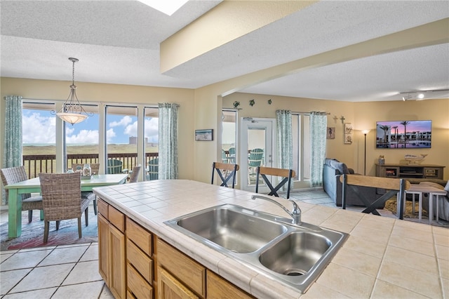 kitchen with tile countertops, sink, decorative light fixtures, and light tile patterned flooring