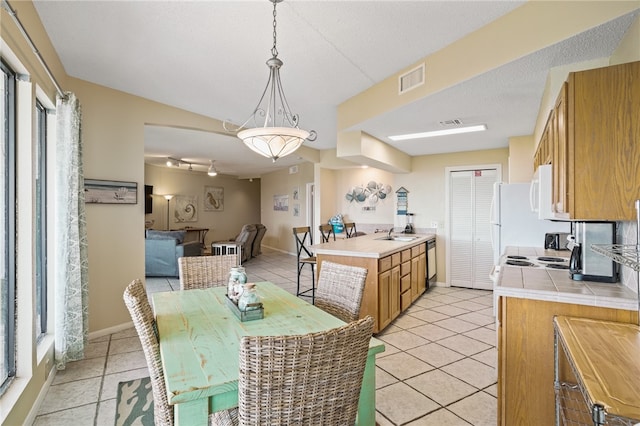 kitchen with light tile patterned floors, pendant lighting, sink, tile counters, and white appliances