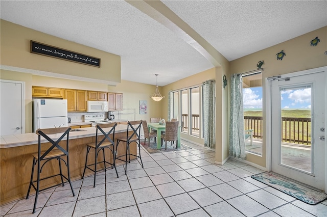 kitchen featuring a kitchen breakfast bar, a textured ceiling, light tile patterned floors, white appliances, and pendant lighting