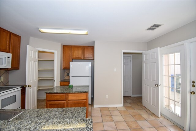 kitchen with a kitchen island, dark stone countertops, white appliances, and light tile patterned floors