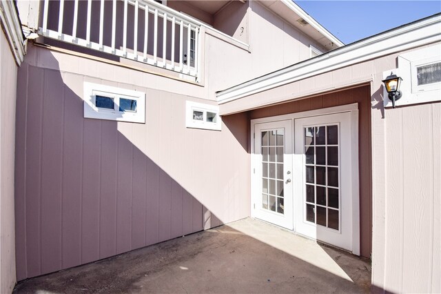 view of exterior entry with french doors, a balcony, and a patio area