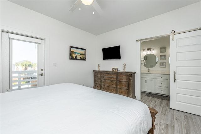 bedroom with access to exterior, light wood-type flooring, ceiling fan, a barn door, and connected bathroom