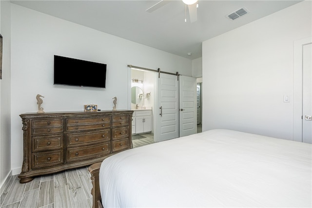 bedroom featuring hardwood / wood-style floors, a barn door, ensuite bathroom, and ceiling fan