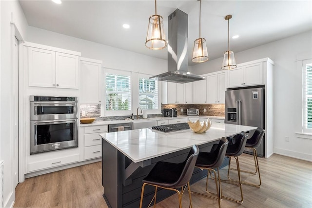 kitchen featuring a center island, decorative light fixtures, appliances with stainless steel finishes, white cabinetry, and island range hood