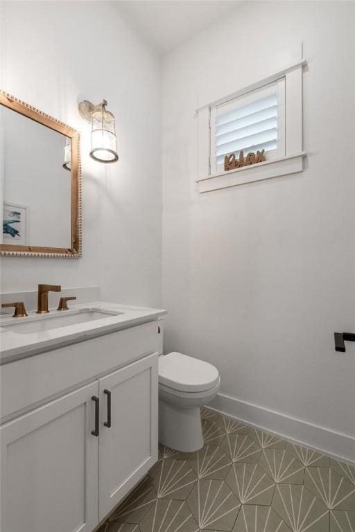 half bathroom with baseboards, vanity, and toilet