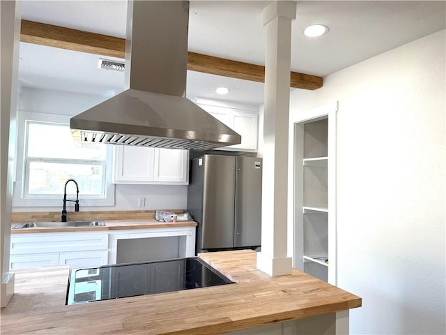 kitchen with sink, stainless steel refrigerator, white cabinetry, black electric stovetop, and island range hood