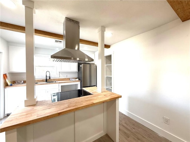 kitchen with sink, island range hood, stainless steel fridge, and wooden counters