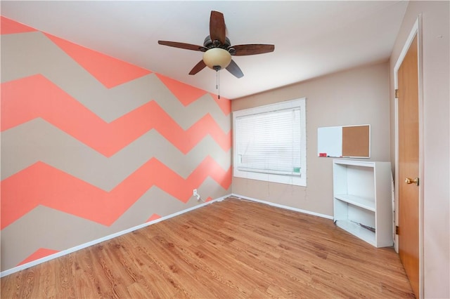 spare room with wood finished floors, a ceiling fan, and baseboards