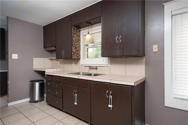 kitchen featuring dark brown cabinetry, light tile patterned floors, backsplash, and a sink