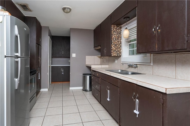 kitchen with a sink, stainless steel appliances, decorative backsplash, light tile patterned flooring, and dark brown cabinets