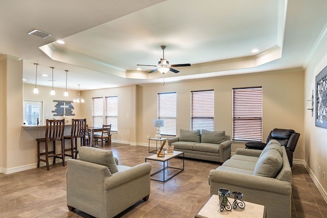 living room featuring a tray ceiling, ornamental molding, and ceiling fan with notable chandelier