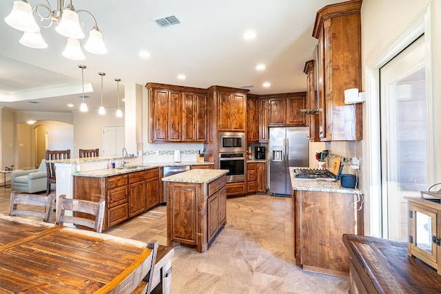 kitchen featuring light stone counters, kitchen peninsula, a kitchen island, appliances with stainless steel finishes, and decorative light fixtures