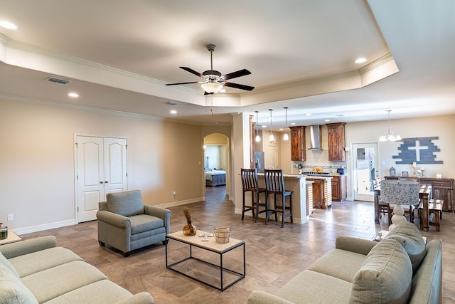 living room featuring ceiling fan with notable chandelier, crown molding, and a tray ceiling