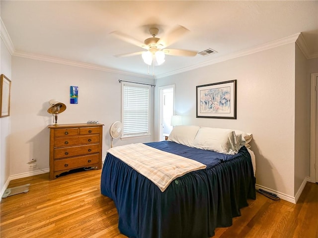 bedroom with ceiling fan, wood finished floors, visible vents, baseboards, and crown molding