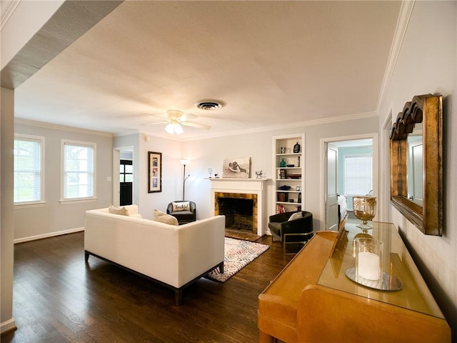 living area with built in features, visible vents, a fireplace with flush hearth, ornamental molding, and dark wood-type flooring