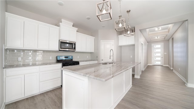 kitchen featuring black gas range oven, a kitchen island with sink, sink, pendant lighting, and white cabinets