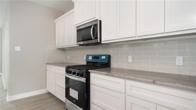 kitchen featuring tasteful backsplash, light stone counters, light hardwood / wood-style floors, white cabinets, and appliances with stainless steel finishes