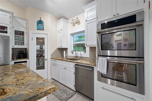 kitchen with stainless steel appliances, dark stone countertops, white cabinetry, and tasteful backsplash