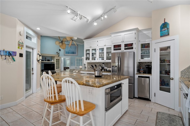 kitchen with white cabinetry, appliances with stainless steel finishes, dark stone counters, backsplash, and lofted ceiling