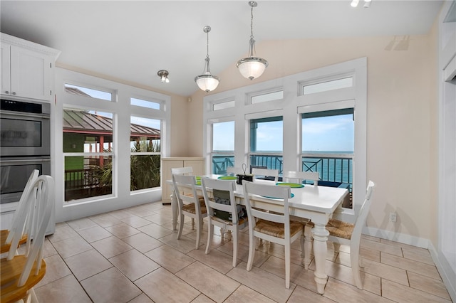 dining area with a wealth of natural light, a water view, vaulted ceiling, and light tile patterned flooring