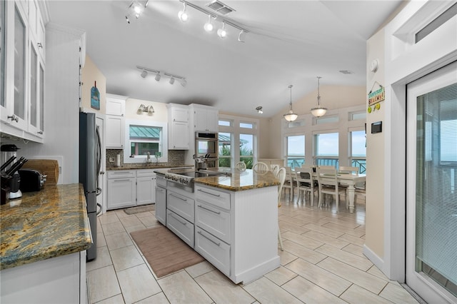 kitchen with a center island with sink, dark stone counters, white cabinetry, a water view, and lofted ceiling