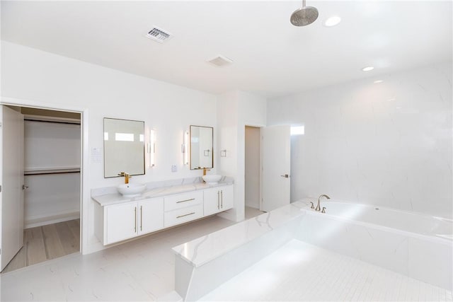 bathroom with double vanity, visible vents, a bath, and a sink