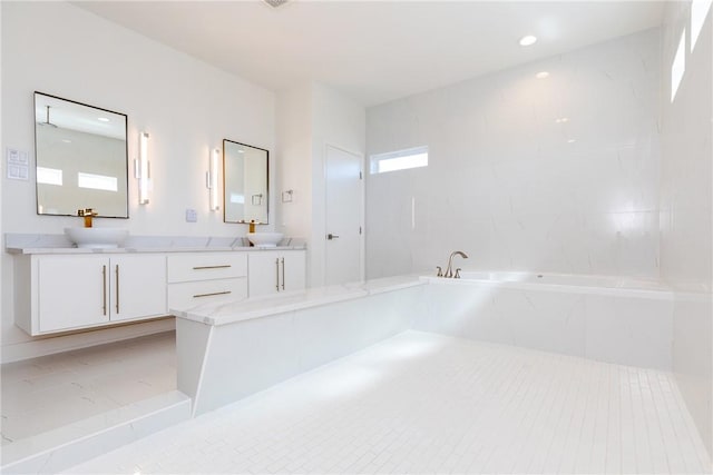 bathroom with double vanity, a garden tub, recessed lighting, and a sink